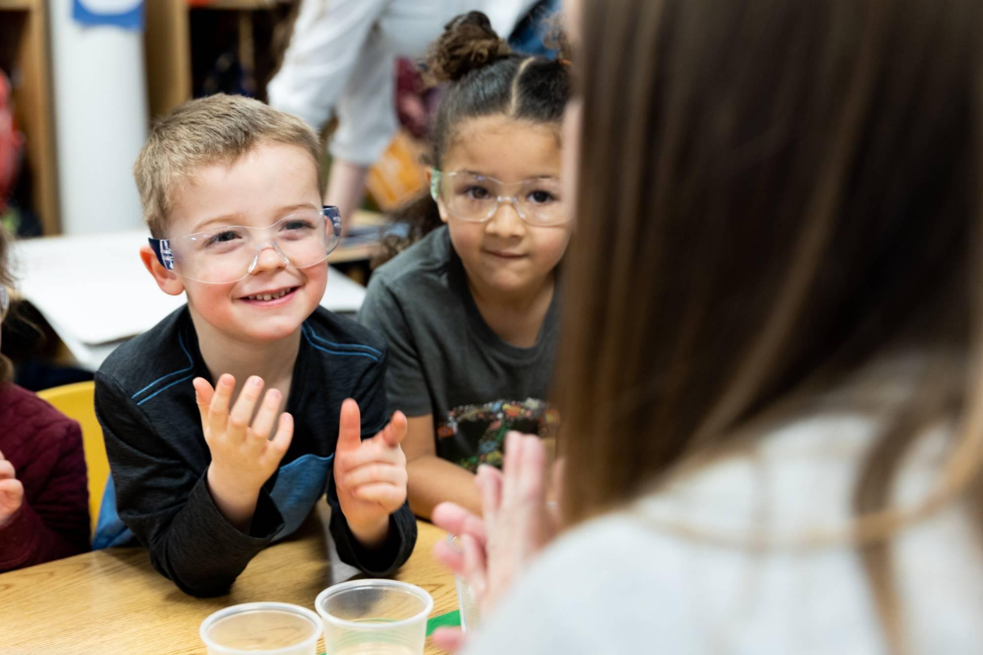 A kid with protective eye wear, smiling, listening to his teacher